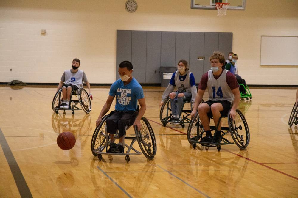 Image 1 of 12 Adults chasing a basketball during a wheelchair basketball game.